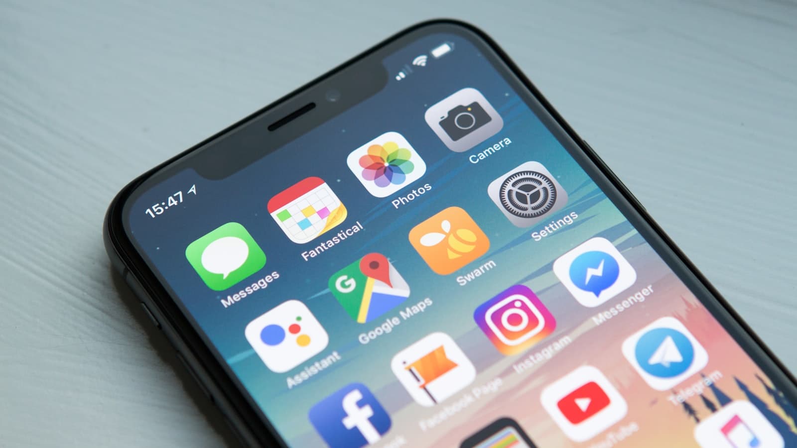 An iPhone home screen on a light wooden desk