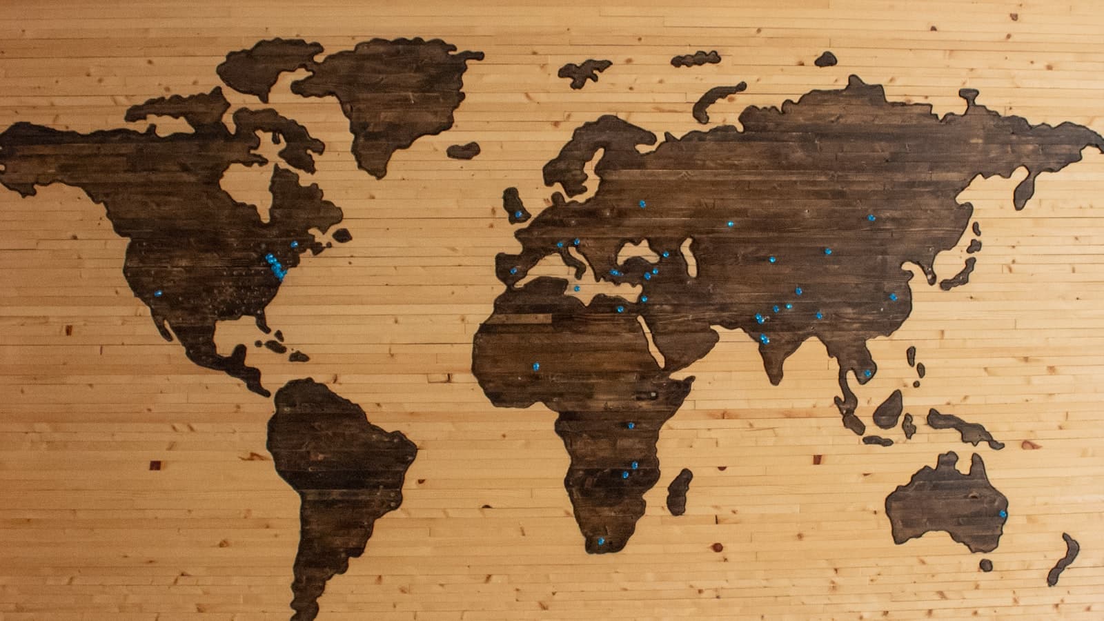 A wooden world map with location pins